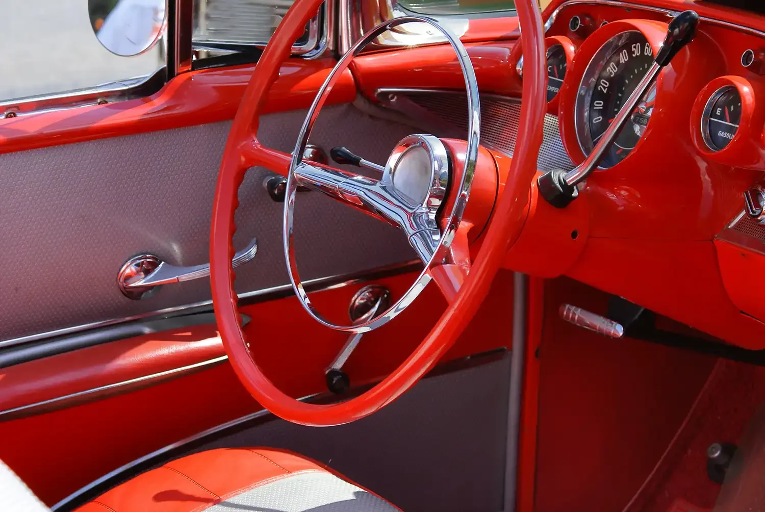 Innenraum eines klassischen roten Oldtimers mit chromfarbenem Lenkrad, rotem Armaturenbrett, Rundinstrumenten und rot-brauner Polsterung im Retro-Stil der 1950er Jahre.