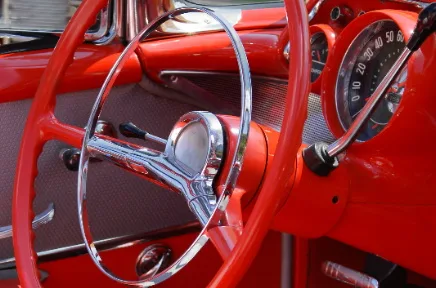 Innenraum eines klassischen roten Oldtimers mit chromfarbenem Lenkrad, Armaturenbrett und Tacho im Retro-Design.