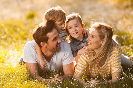 Eine glückliche vierköpfige Familie liegt lächelnd in einer sonnigen Blumenwiese und genießt gemeinsam Zeit in der Natur.