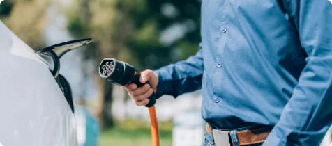 Person lädt ein Elektroauto an einer Ladestation auf, während sie ein blaues Hemd trägt und im Freien steht.